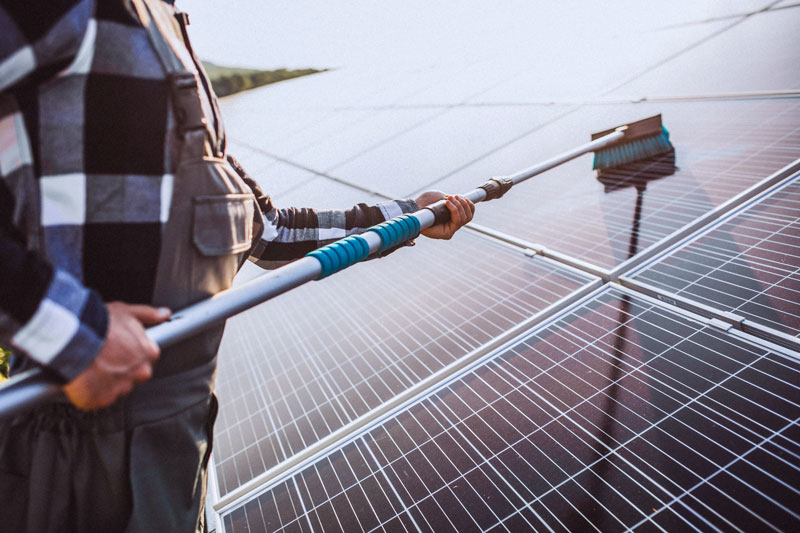 Solarreinigung Frankfurt - Fachkraft reinigt Solarpanels auf Dach mit Teleskop Wasserbürste für maximale Leistung